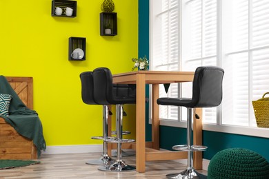 Image of Wooden dining table and chairs in room. Interior design with yellow and teal walls