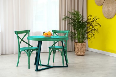 Image of Turquoise dining table and chairs near yellow wall in room. Interior design