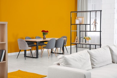 Image of Dining table and chairs near orange wall in room. Interior design