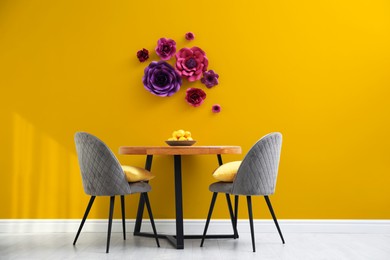 Image of Dining table and grey chairs near orange wall with floral decor in room. Interior design