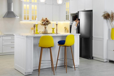 Image of Dining table and yellow chairs in kitchen. Interior design with color accent. Woman near refrigerator