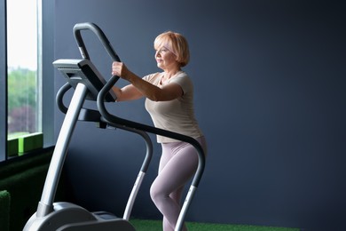 Photo of Senior woman training on elliptical machine in gym