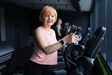 Photo of Senior woman training on elliptical machine in gym