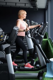 Photo of Senior woman training on elliptical machine in gym