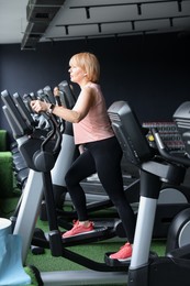 Photo of Senior woman training on elliptical machine in gym