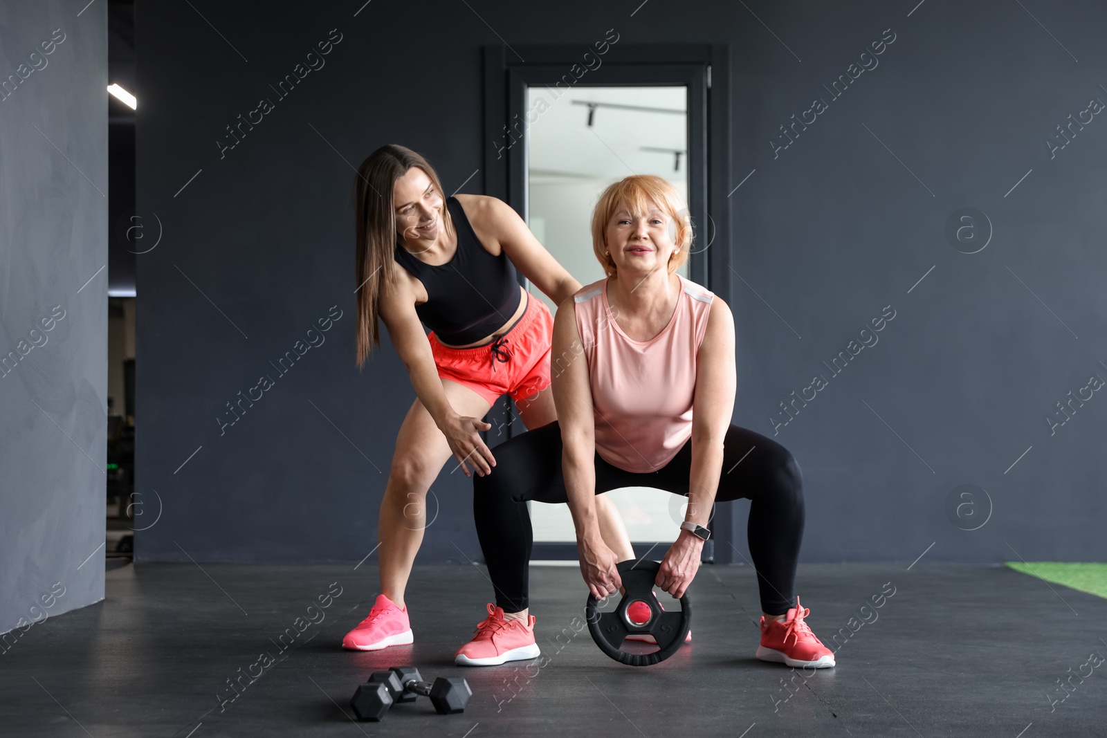 Senior woman training with weight plate supervised by professional trainer in gym Photo of Senior woman training with weight plate supervised by professional trainer in gym