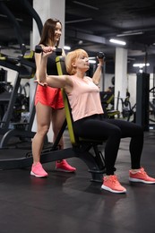 Photo of Senior woman training with dumbbells supervised by professional trainer in gym