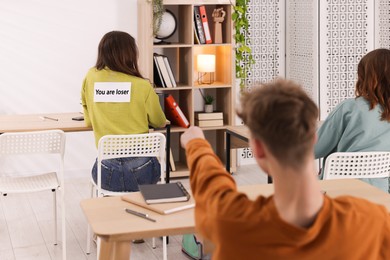 Photo of Schoolmates bullying teenage girl with sign You Loser on her back at school