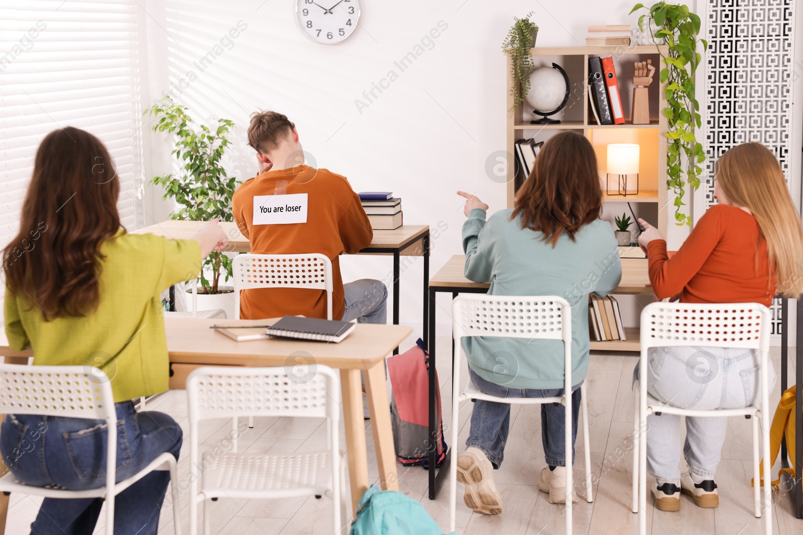 Schoolmates bullying teenage boy with sign You Loser on his back at school Photo of Schoolmates bullying teenage boy with sign You Loser on his back at school