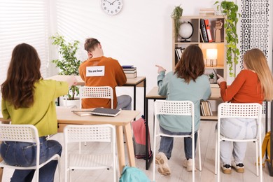 Photo of Schoolmates bullying teenage boy with sign You Loser on his back at school