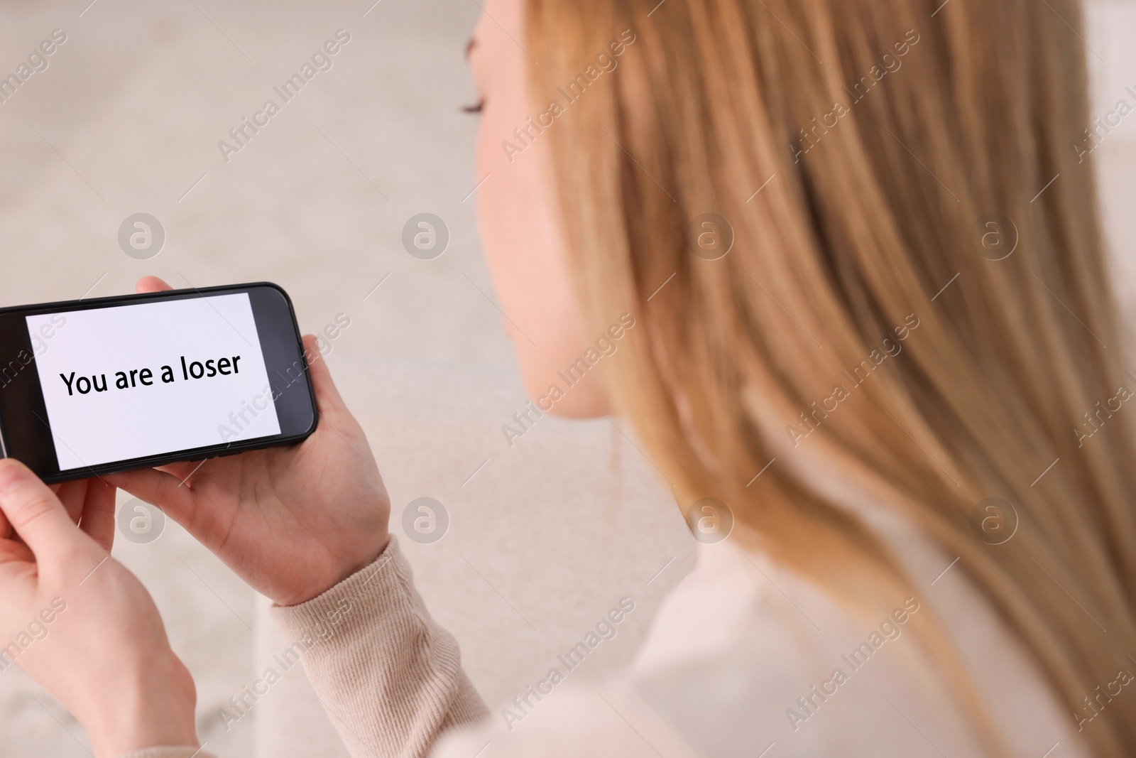 Cyber bullying. Upset teenage girl looking at smartphone with text You Loser at home, closeup Photo of Cyber bullying. Upset teenage girl looking at smartphone with text You Loser at home, closeup