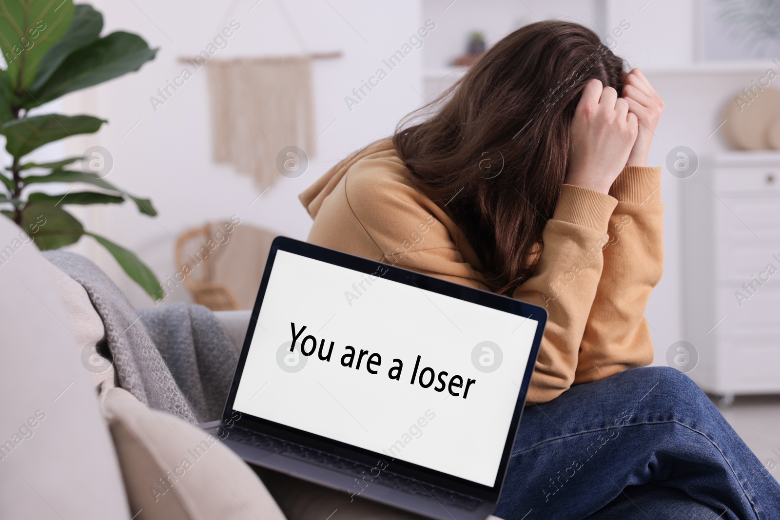 Cyber bullying. Upset teenage girl and laptop with text You Loser on sofa at home Photo of Cyber bullying. Upset teenage girl and laptop with text You Loser on sofa at home
