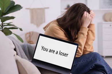 Photo of Cyber bullying. Upset teenage girl and laptop with text You Loser on sofa at home