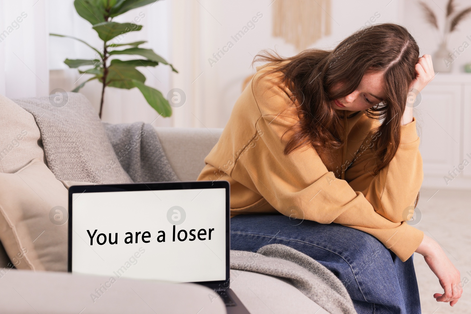 Cyber bullying. Upset teenage girl and laptop with text You Loser on sofa at home Photo of Cyber bullying. Upset teenage girl and laptop with text You Loser on sofa at home