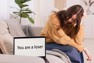 Photo of Cyber bullying. Upset teenage girl and laptop with text You Loser on sofa at home