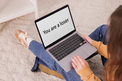Photo of Cyber bullying. Upset teenage girl and laptop with text You Loser on floor indoors, closeup