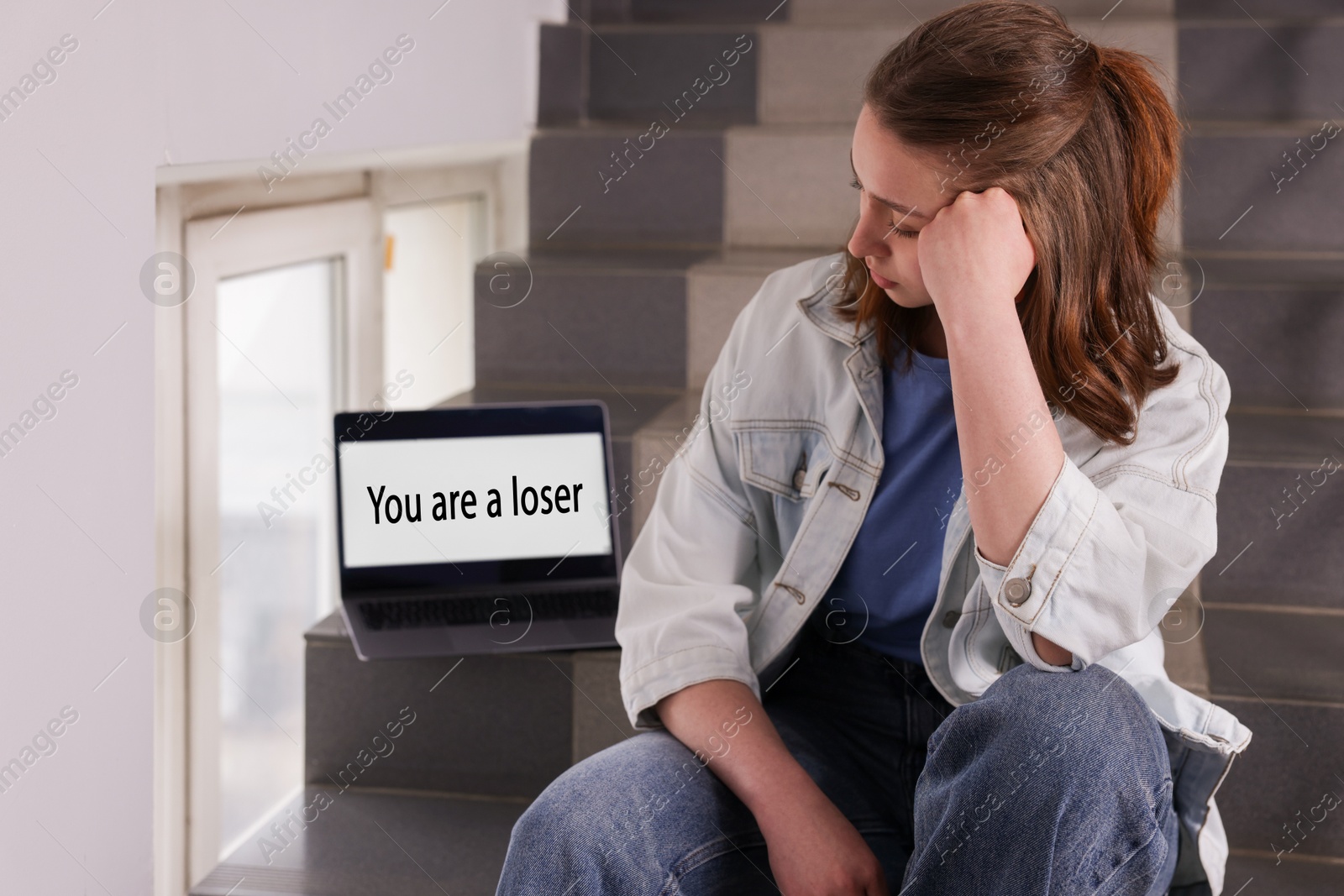 Cyber bullying. Upset teenage girl and laptop with text You Loser on stairs indoors Photo of Cyber bullying. Upset teenage girl and laptop with text You Loser on stairs indoors