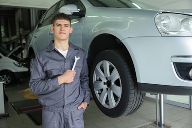Photo of Professional mechanic with wrench near lifted car in garage