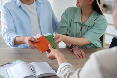 Photo of Travel agent giving passports with tickets to couple at wooden table in office, closeup