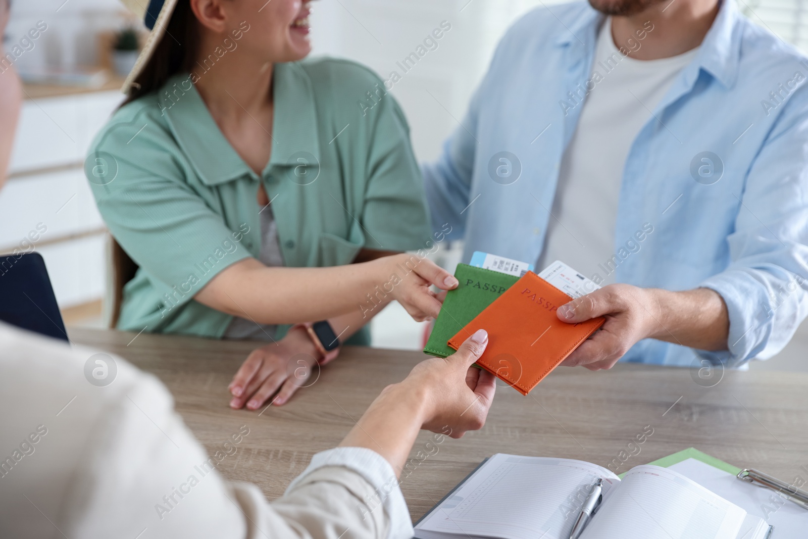 Travel agent giving passports with tickets to couple at wooden table in office, closeup Photo of Travel agent giving passports with tickets to couple at wooden table in office, closeup