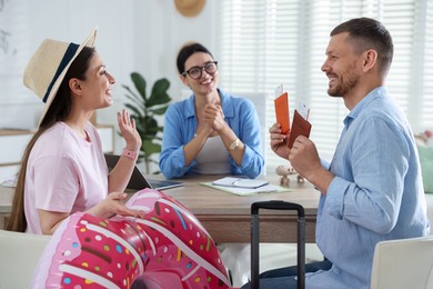 Photo of Happy couple planning vacation with travel agent at wooden table in office, selective focus