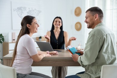Photo of Happy couple planning vacation with travel agent at wooden table in office