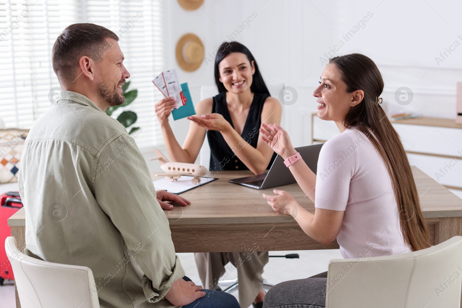Happy couple planning vacation with travel agent at wooden table in office Photo of Happy couple planning vacation with travel agent at wooden table in office