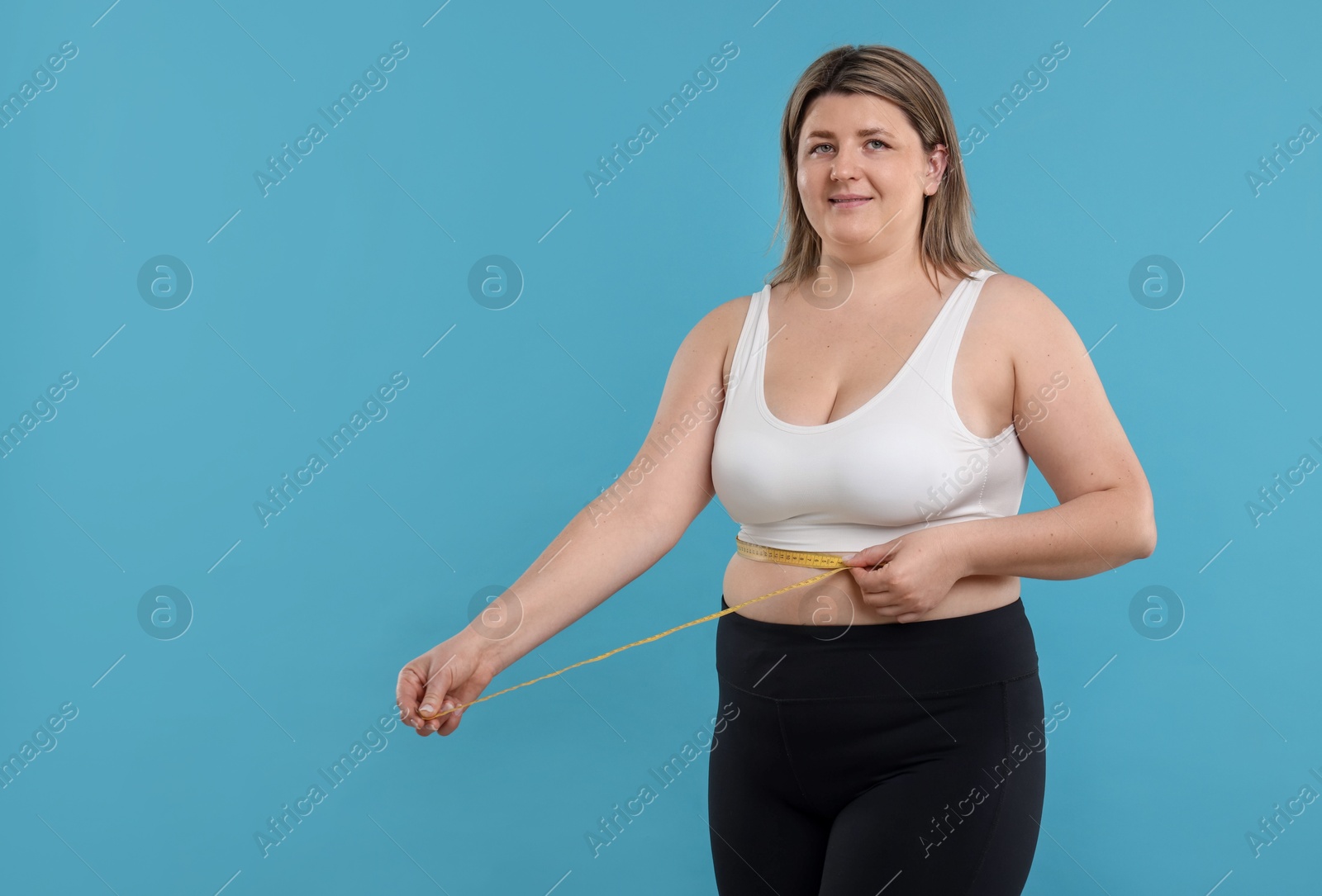 Weight loss. Plus size woman measuring waist with tape on light blue background Photo of Weight loss. Plus size woman measuring waist with tape on light blue background