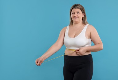 Photo of Weight loss. Plus size woman measuring waist with tape on light blue background