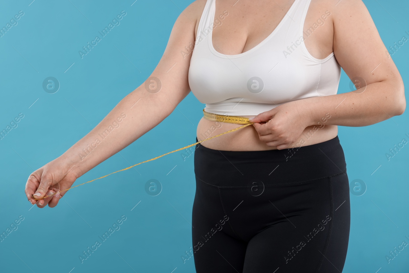 Photo of Weight loss. Plus size woman measuring waist with tape on light blue background, closeup