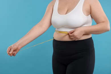 Photo of Weight loss. Plus size woman measuring waist with tape on light blue background, closeup