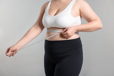 Photo of Weight loss. Plus size woman measuring waist with tape on gray background, closeup