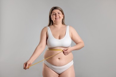 Photo of Weight loss. Plus size woman measuring waist with tape on gray background