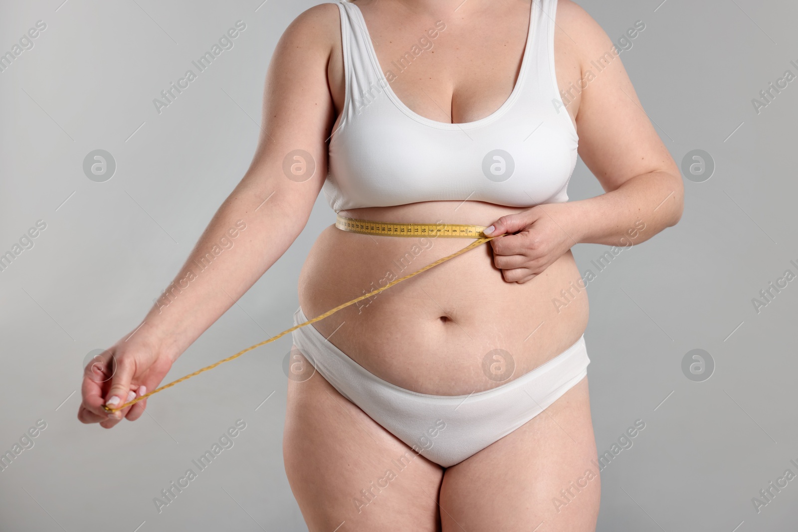 Weight loss. Plus size woman measuring waist with tape on gray background, closeup Photo of Weight loss. Plus size woman measuring waist with tape on gray background, closeup