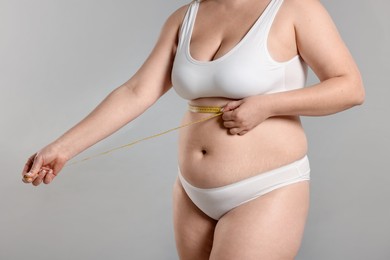 Photo of Weight loss. Plus size woman measuring waist with tape on gray background, closeup