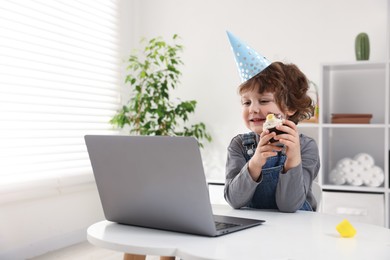 Photo of Birthday celebration. Little boy with cupcake having video call via laptop at table indoors. Space for text
