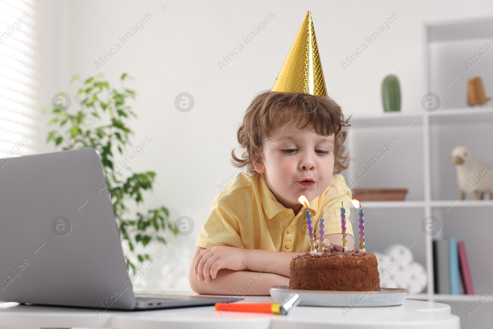 Birthday celebration. Little boy blowing candles on cake while having video call via laptop at table indoors Photo of Birthday celebration. Little boy blowing candles on cake while having video call via laptop at table indoors