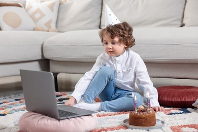 Photo of Birthday celebration. Little boy with cake having video call via laptop at home