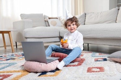 Photo of Birthday celebration. Little boy with cupcake having video call via laptop at home