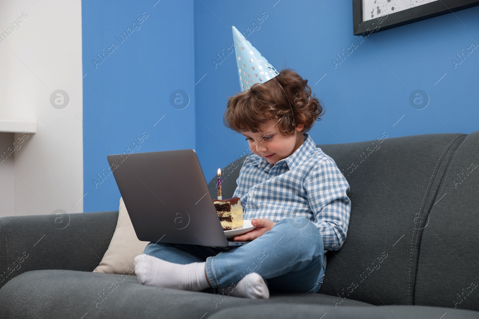 Birthday celebration. Little boy with piece of cake having video call via laptop on sofa at home Photo of Birthday celebration. Little boy with piece of cake having video call via laptop on sofa at home