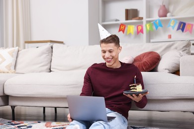 Photo of Man with piece of cake celebrating his birthday and having video call via laptop at home
