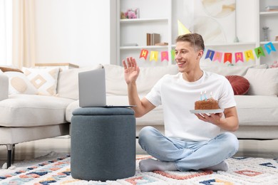 Photo of Man with cake celebrating his birthday and having video call via laptop at home