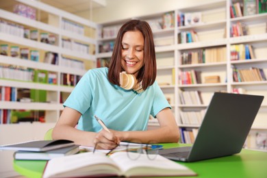 Photo of Student with laptop studying at table in library