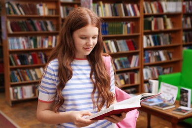 Photo of Student with book and backpack in library