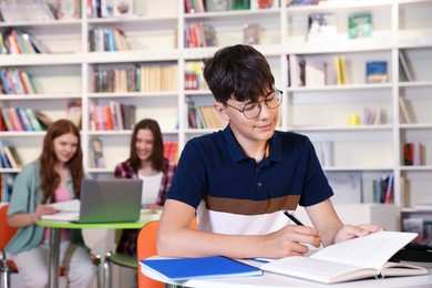 Photo of Student with books studying at table in library