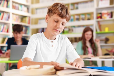 Photo of Student with books studying at table in library