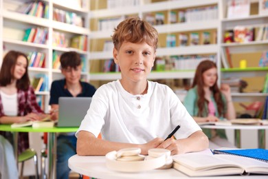 Photo of Student with books studying at table in library