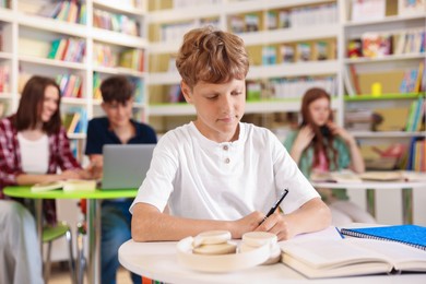 Photo of Student with books studying at table in library