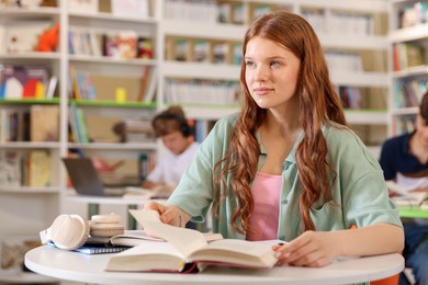 Photo of Student with books studying at table in library