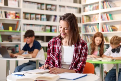 Photo of Student with books studying at table in library